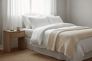 Crisp white linen bedding with waffle blanket and wooden nightstand styled for calm, restful sleep — Flatiron Home
