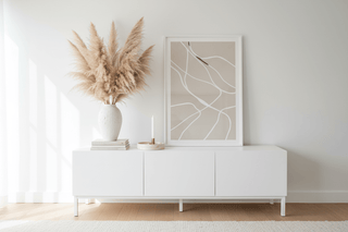 Calm home decor vignette with ceramic vase, pampas grass, travertine tray, and minimal art print on white sideboard — Flatiron Home